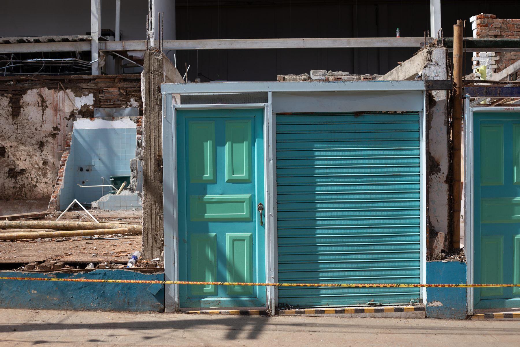 Turquoise shop doors and shutters left standing in front of a gutted interior, hazard tape strung across the front